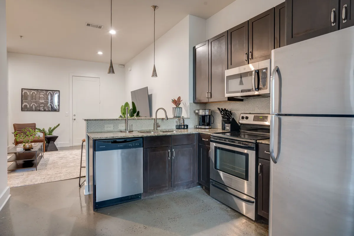 This image showcases a modern kitchen with stainless steel appliances, dark cabinetry, and decorative plants. The atmosphere is both welcoming and functional, clearly suited for cooking, entertaining, or enjoying a solo breakfast. Key features such as the gleaming appliances and open layout are visible, aligning with the section’s focus on culinary creativity.