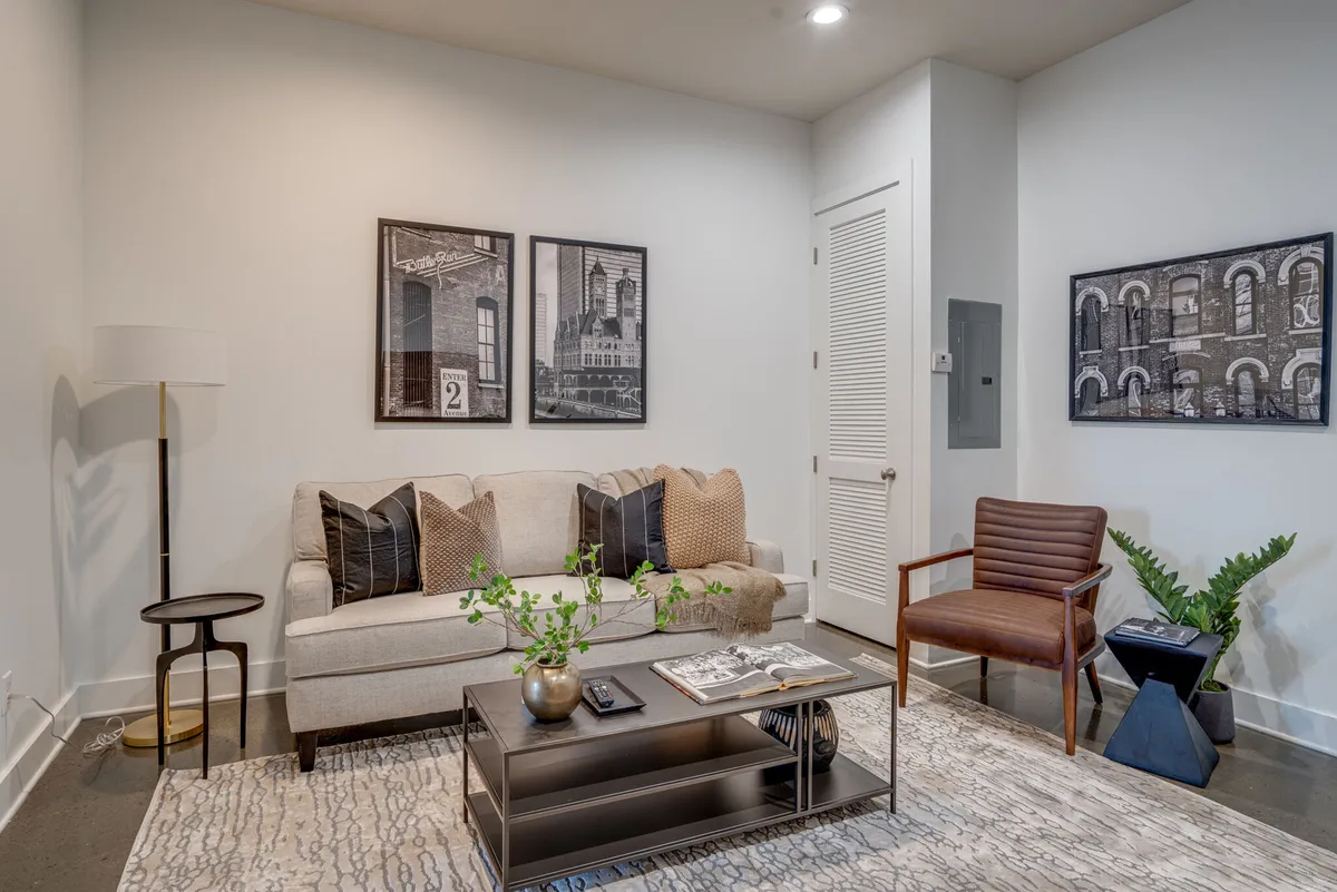 A comfortable, contemporary living area with a sofa, coffee table, artwork on the walls, floor lamp, and a plant. The arrangement is ideal for laid-back gatherings, reading, or enjoying quiet moments.