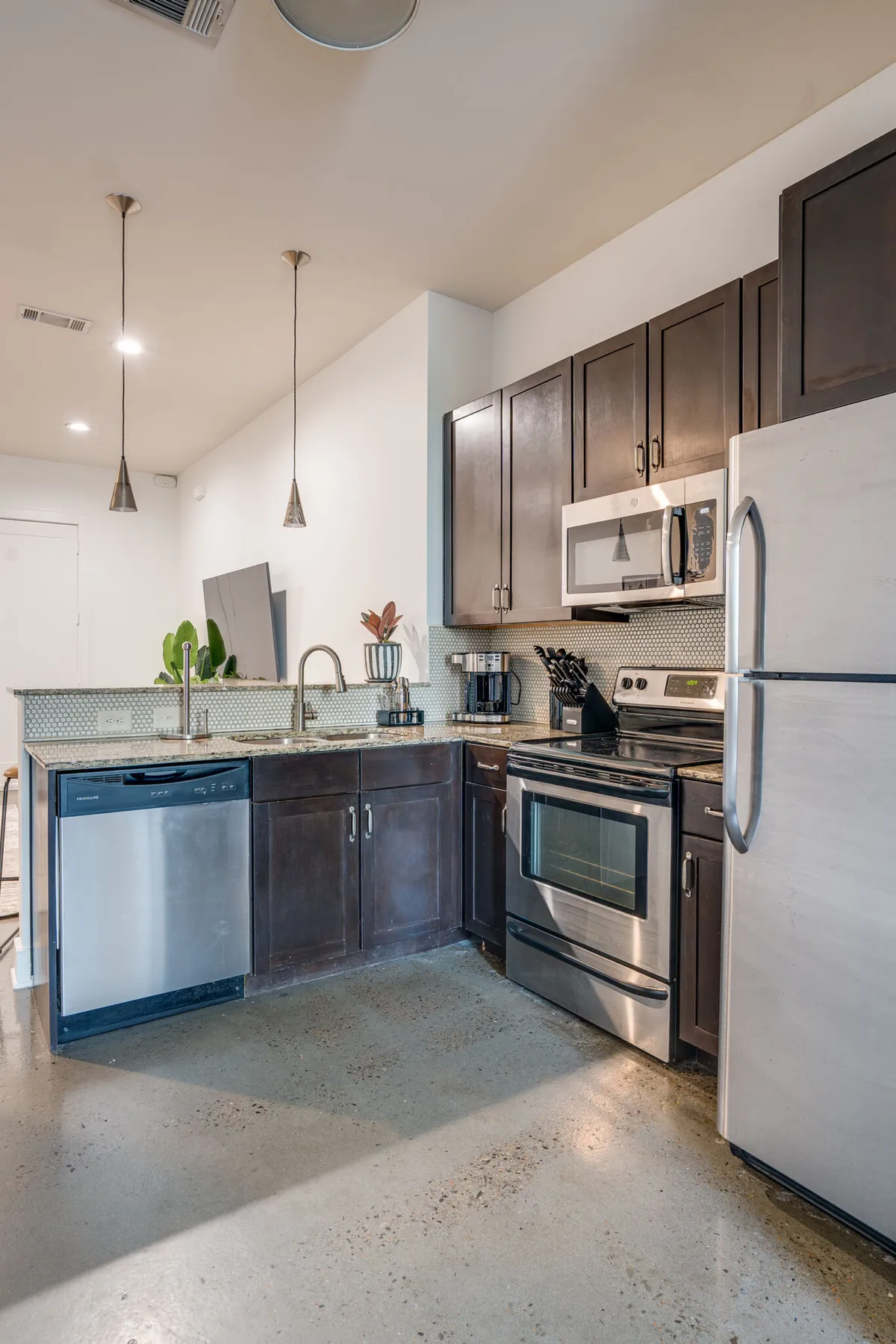 Featuring stainless steel appliances, dark cabinetry, a granite countertop, and elegant pendant lights, this kitchen exudes a contemporary yet inviting vibe. The setup is ideal for both cooking and entertaining, with enough style to inspire culinary creativity.