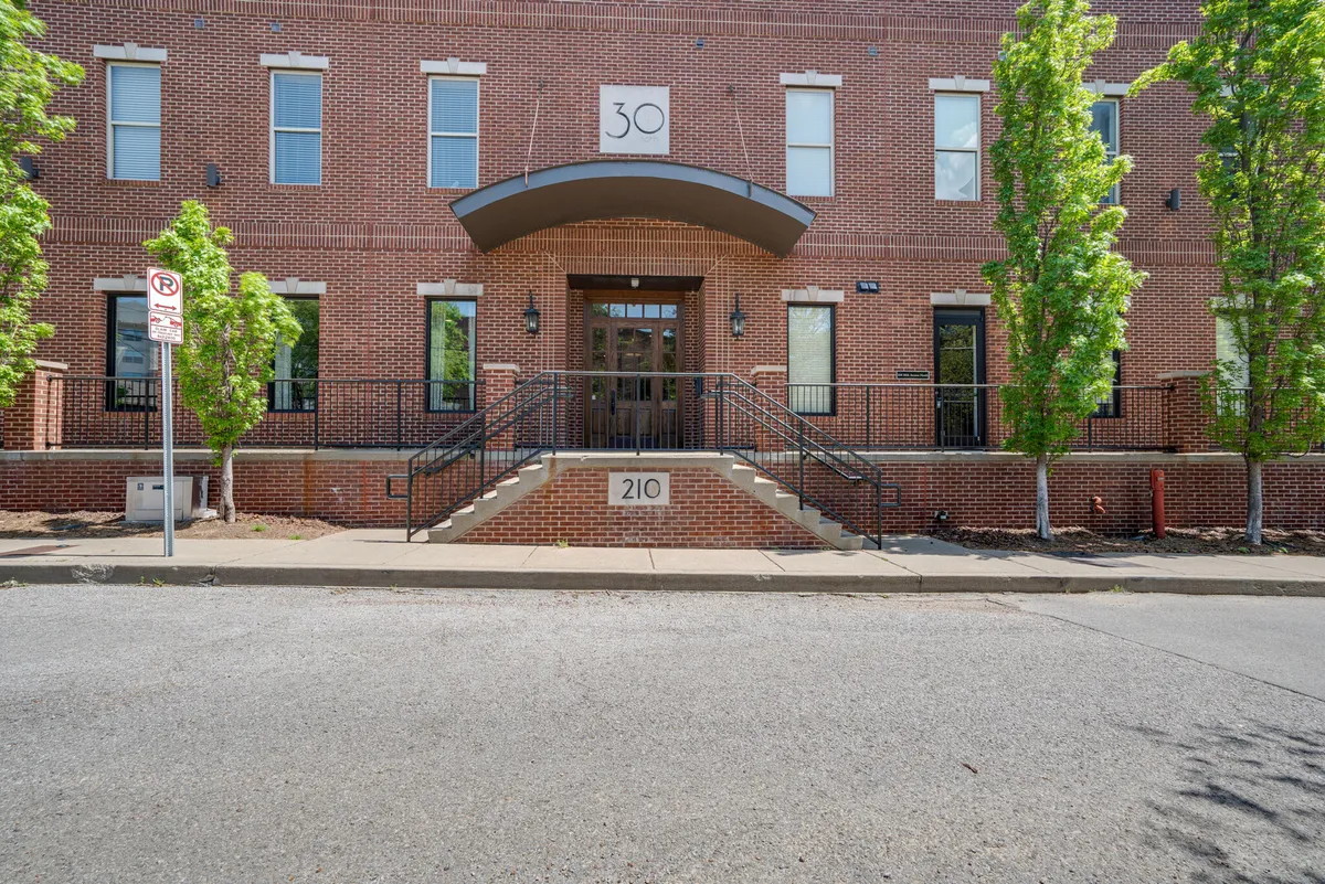 This image features the main entrance of the building, clearly marked with the number 30 and surrounded by thoughtful landscaping. The entrance is welcoming, with people gathering on the steps, suggesting a communal and friendly environment.