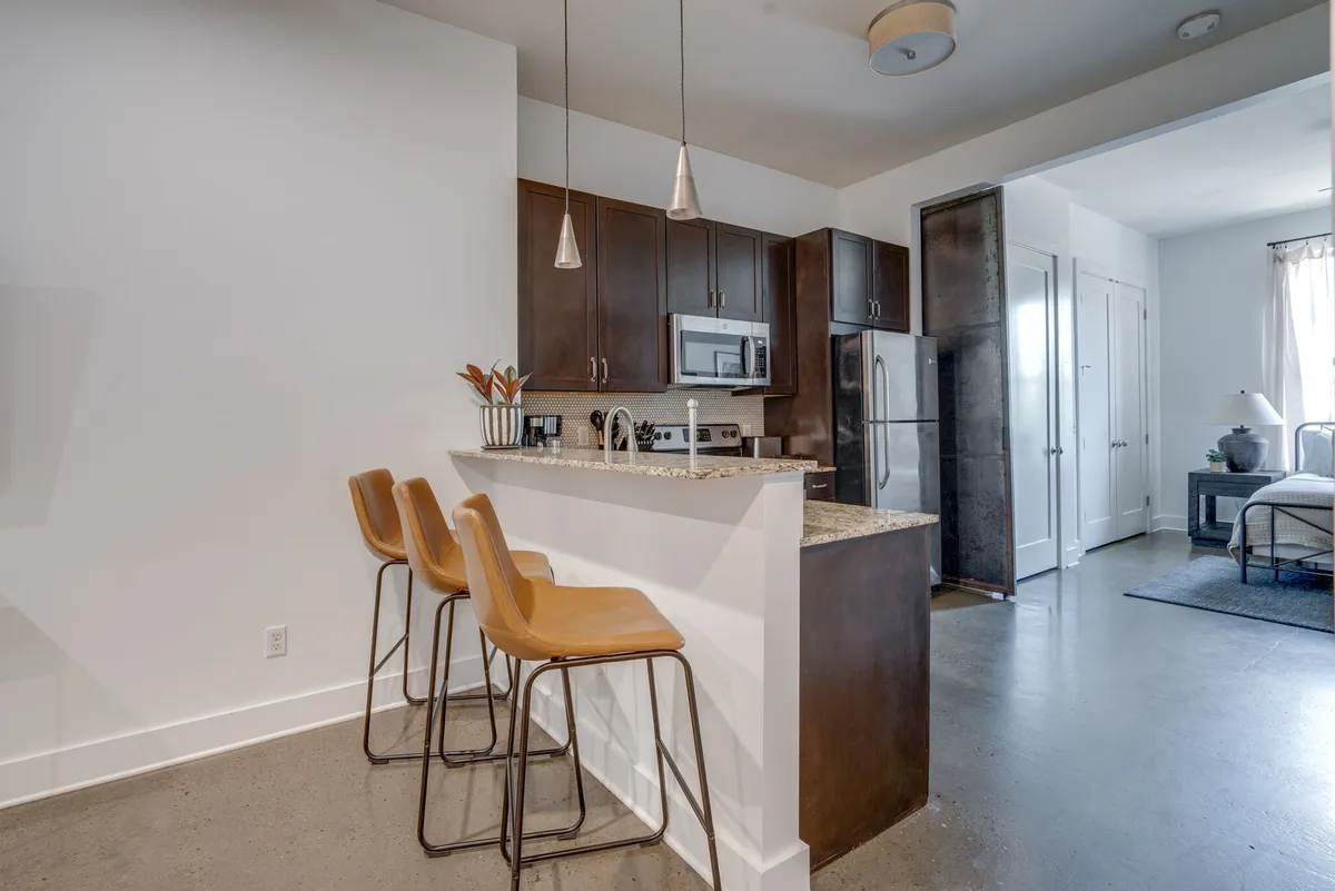 A bright, inviting kitchen scene with a substantial island, bar stools, and visible appliances. The layout encourages socializing while cooking or enjoying a quick bite, with ample space for group activities or gatherings. The design blends functionality with a homely touch.